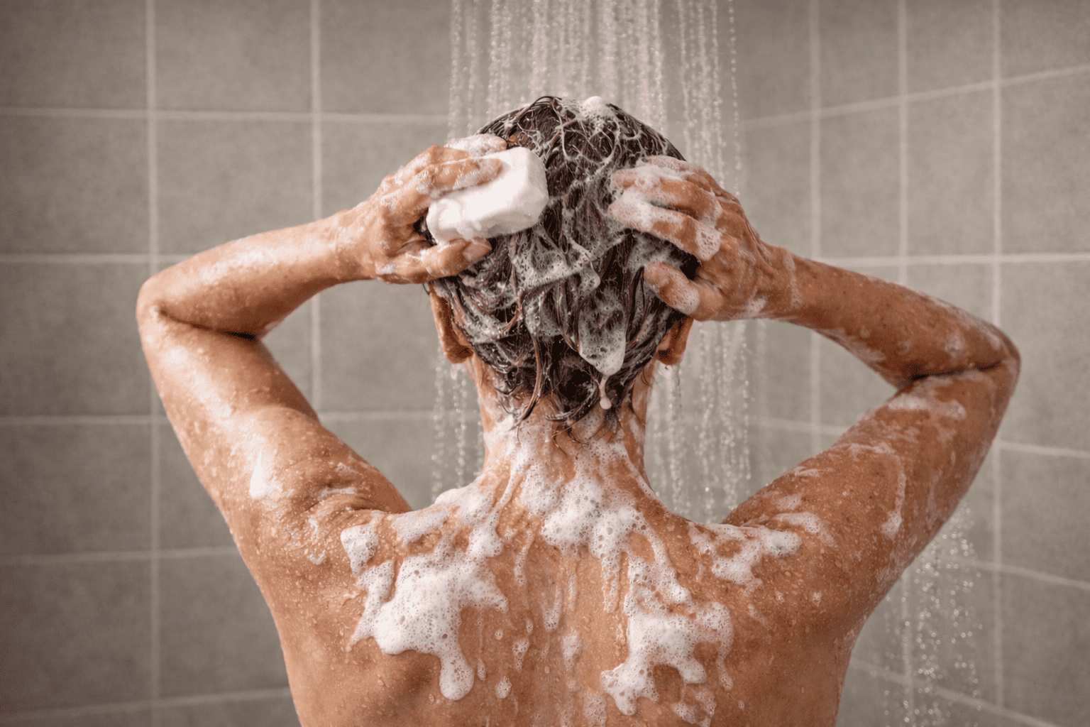 Persona lavándose el pelo con champú sólido en la ducha